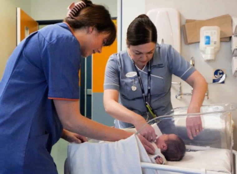 A midwife and nurse attending to a baby in a cot.